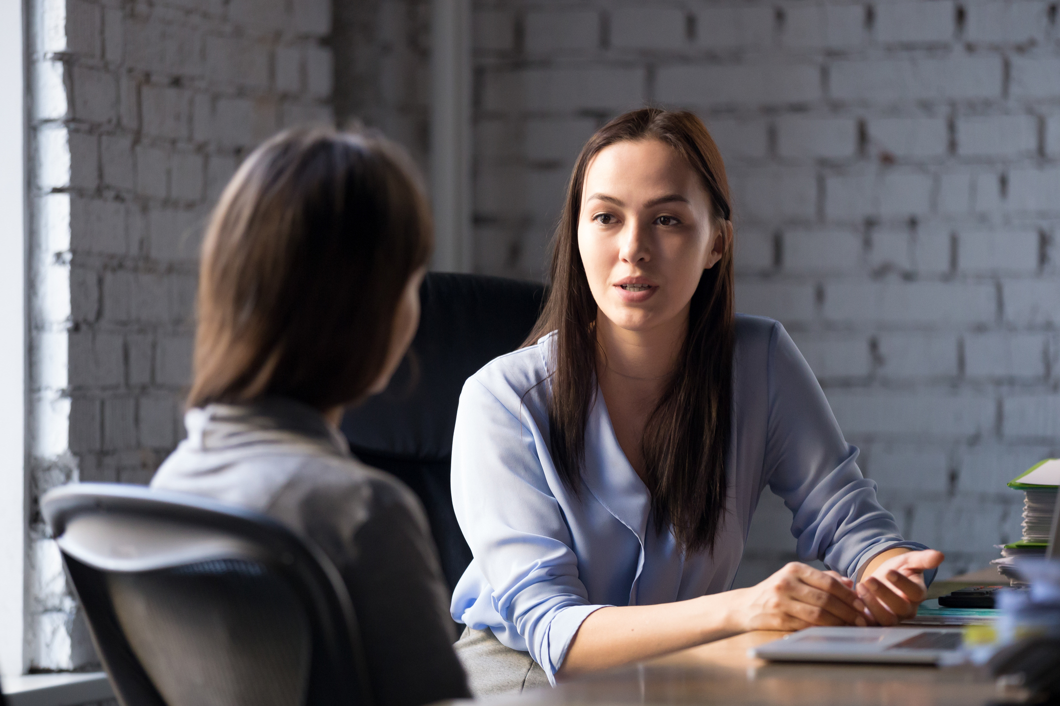 Serious professional female employee consulting boss at meeting to discuss the news of her pregnancy.