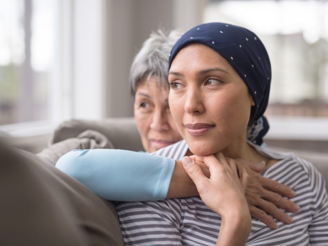 An Ashkenazi Jewish woman wearing a headscarf and fighting breast cancer sits on the couch with her mother. 