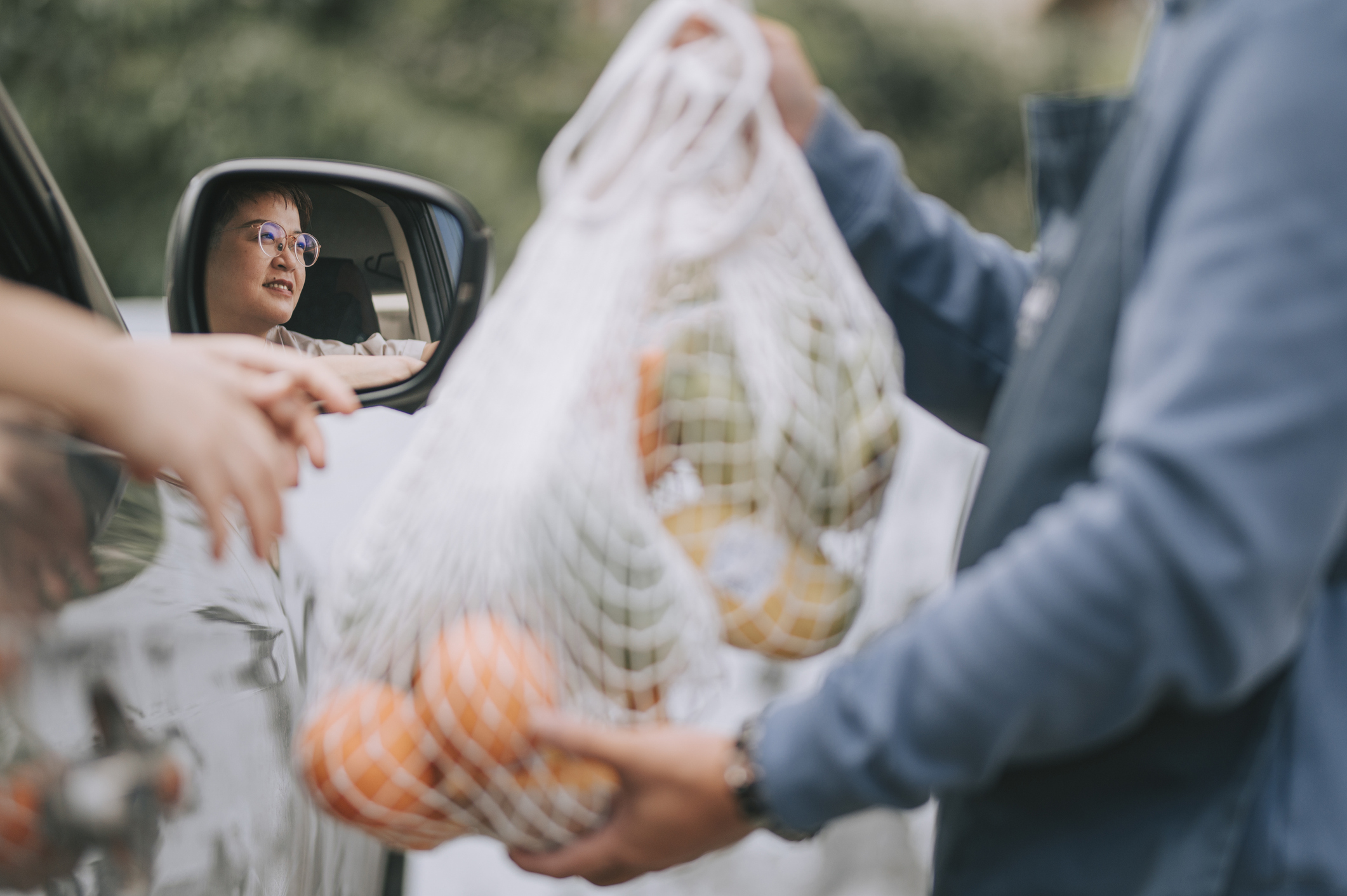 Woman in car recieves fresh produce and food to avoid with fibroids from car-side attendant at grocery store.